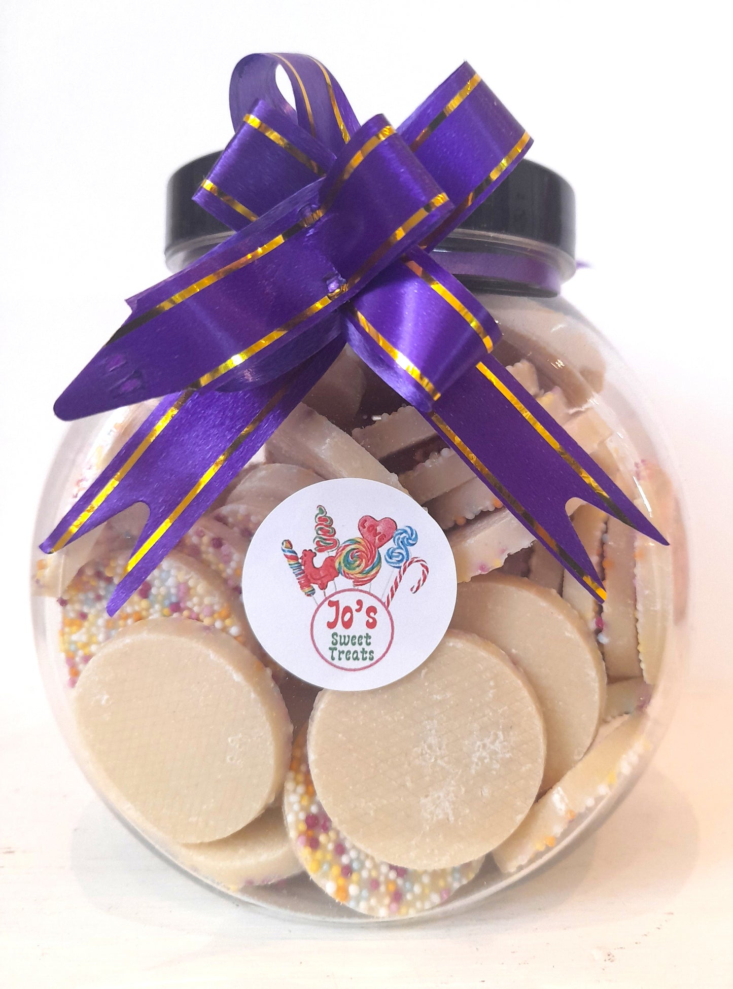 A clear jar filled with rwhite chocolate jazzies adorned with a purple ribbon bow on top
