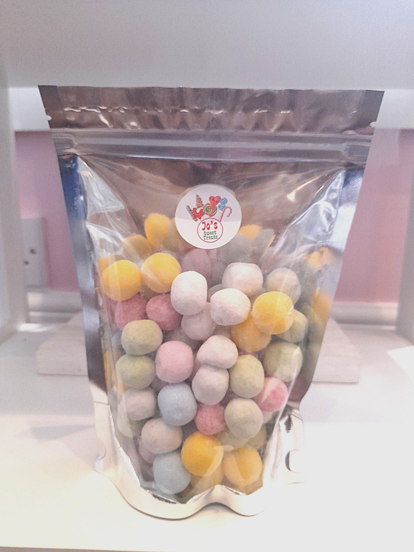 A clear plastic pouch filled with mixed bon bons, which are round sugar candies in various colors including pink, yellow, and green.
