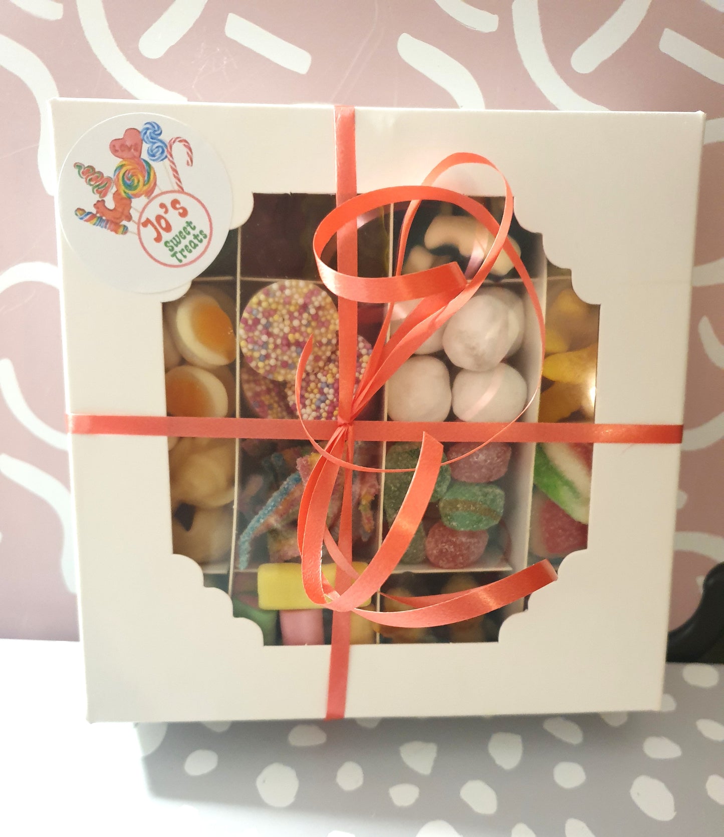 Box of assorted candies with a red ribbon on a patterned background