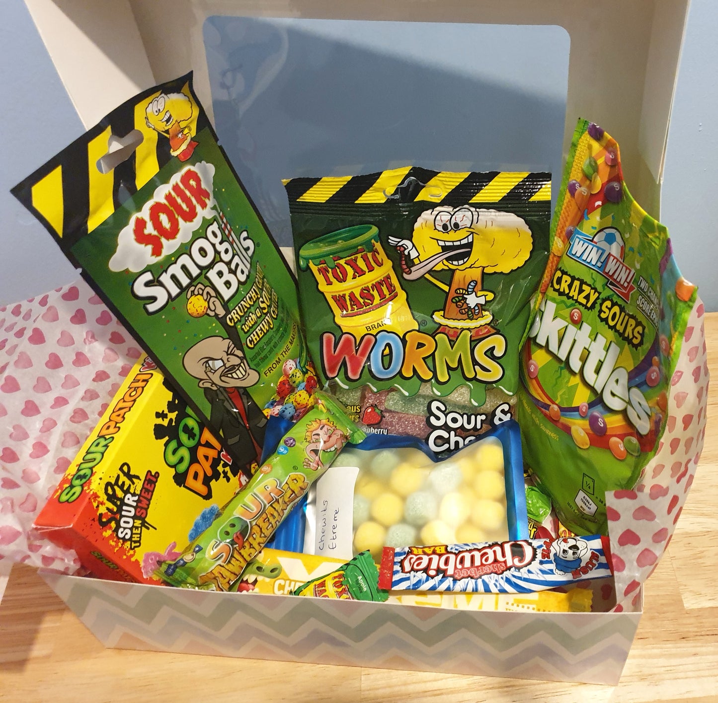 Assorted sour candy packages in a box on a wooden surface