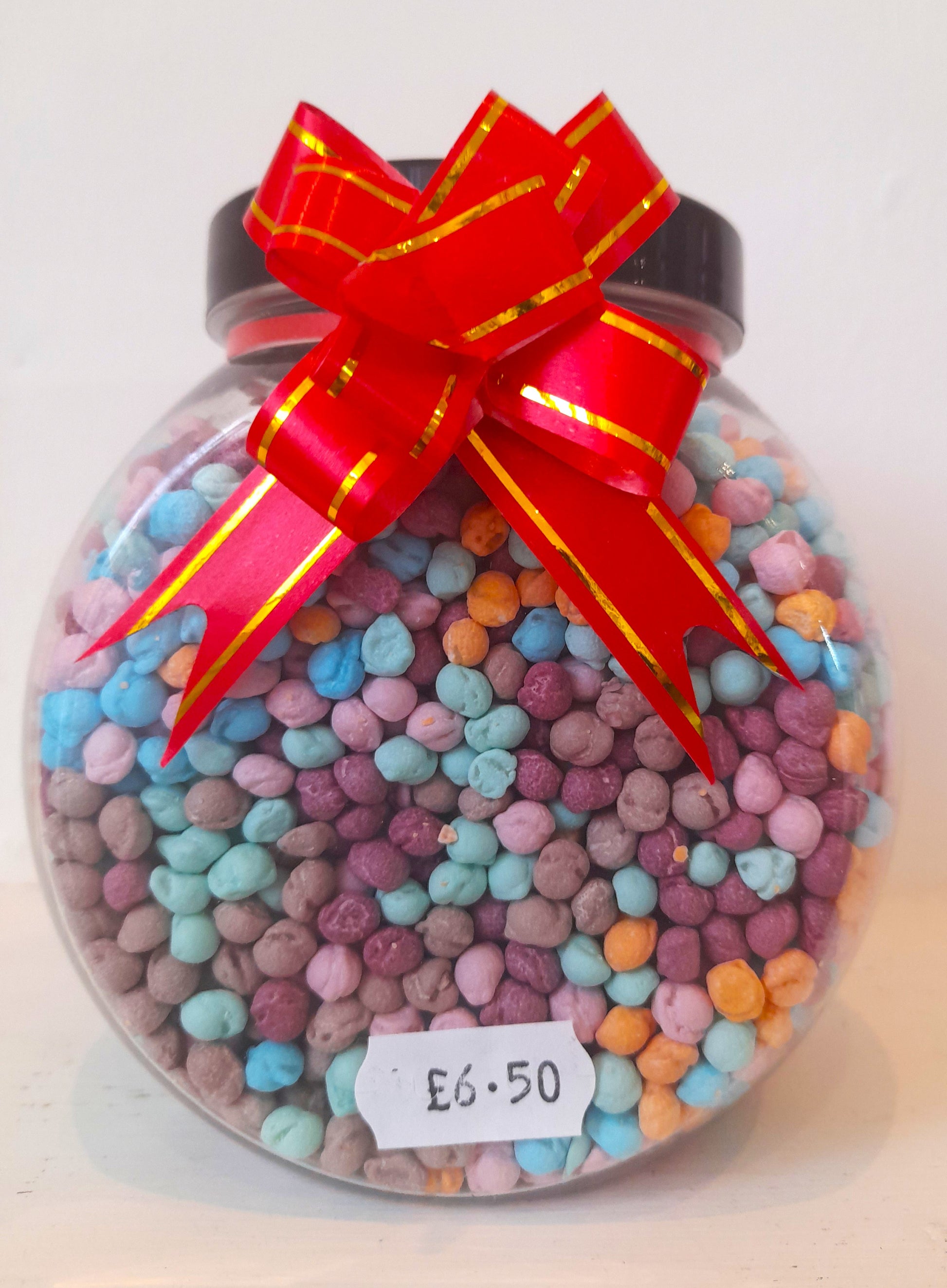 A clear jar filled with multicolored millions candy, adorned with a red ribbon and a label with a price tag.