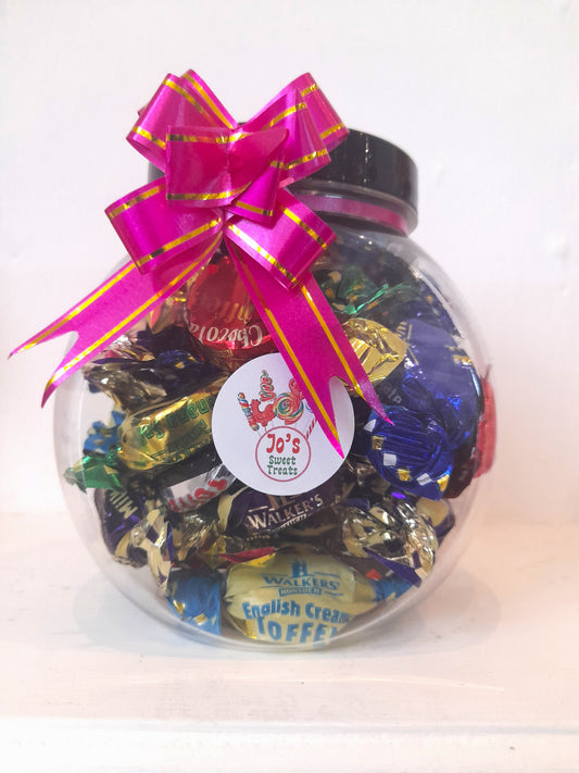 A clear toffee jar filled with assorted candies, adorned with a pink and yellow ribbon bow on top.