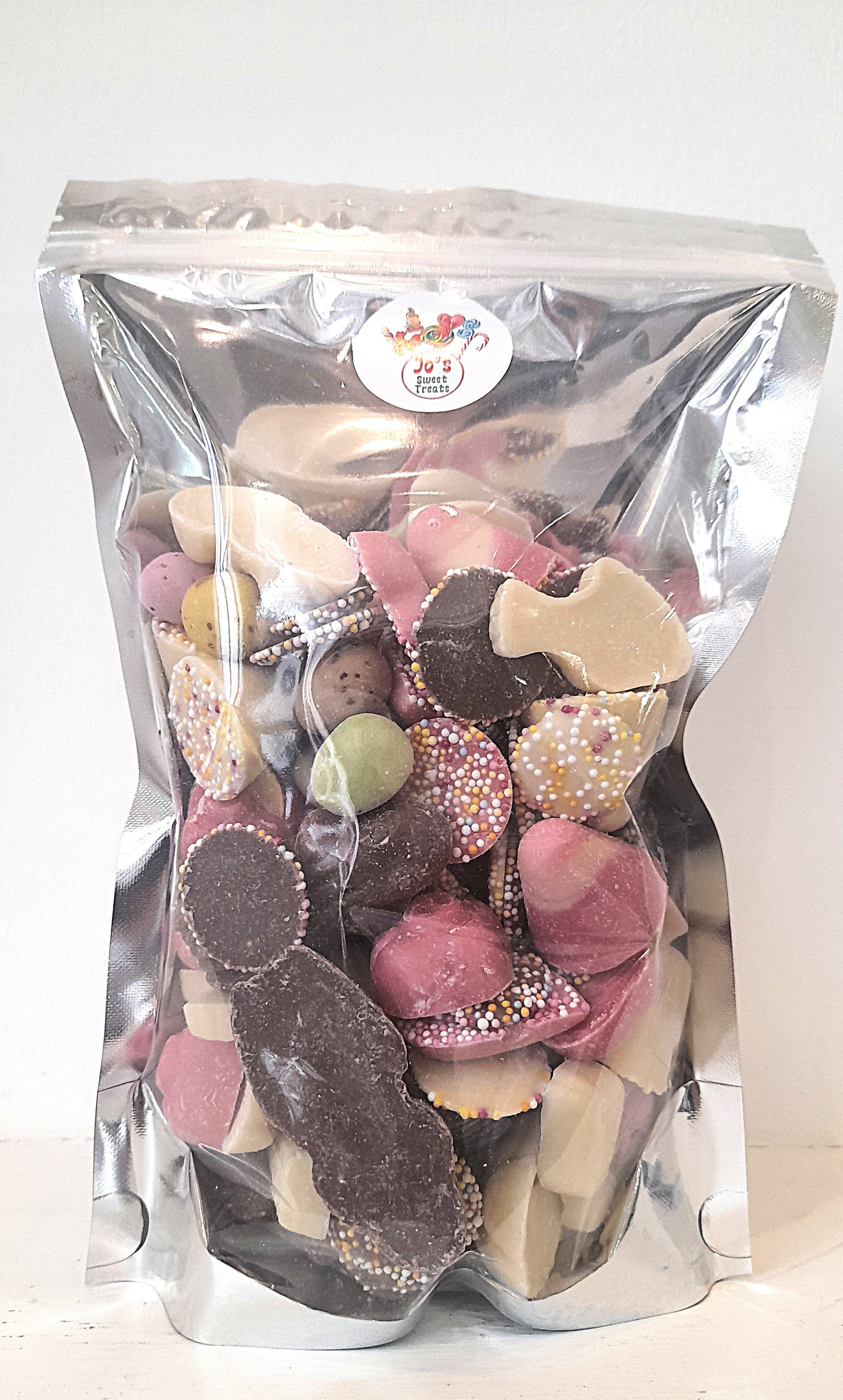 A clear plastic bag filled with various shapes of chocolate pieces, including hearts, circles, and other candies. The bag is labeled with the brand 'Jo's Sweet Treats'.