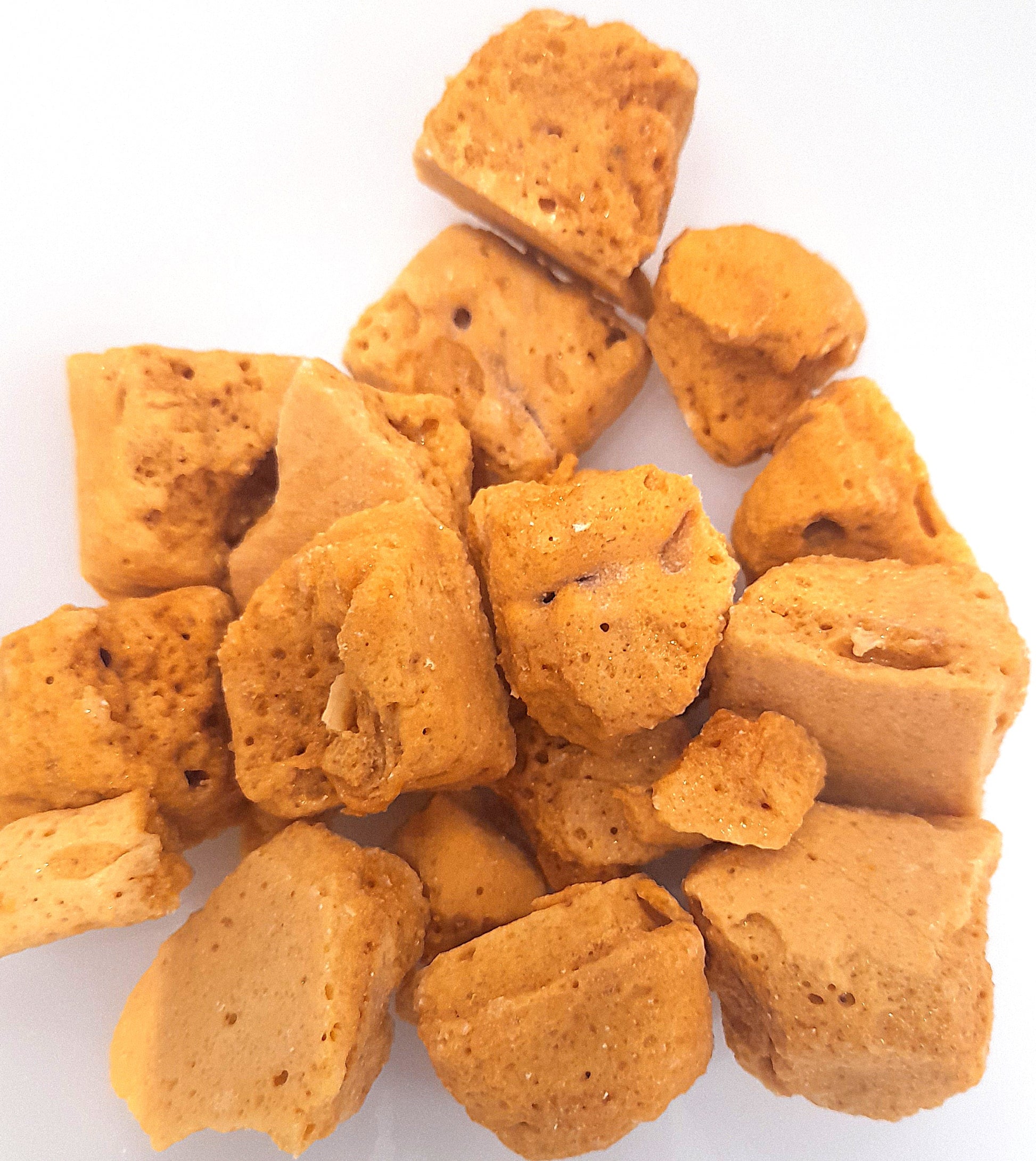 A pile of light brown honeycomb cinder toffee pieces on a white plate.