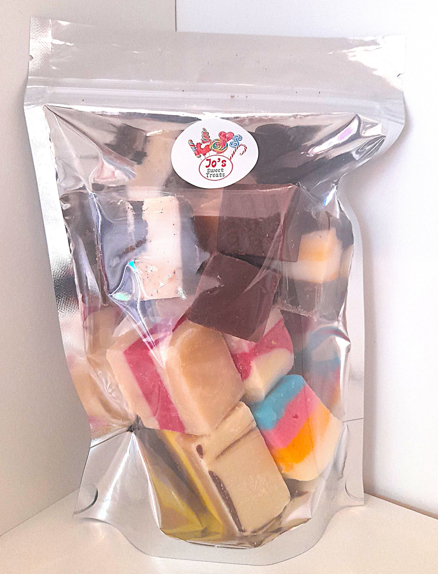 A clear plastic pouch filled with assorted colorful fudge pieces, sealed with a label showing the product name and an image of the fudge.