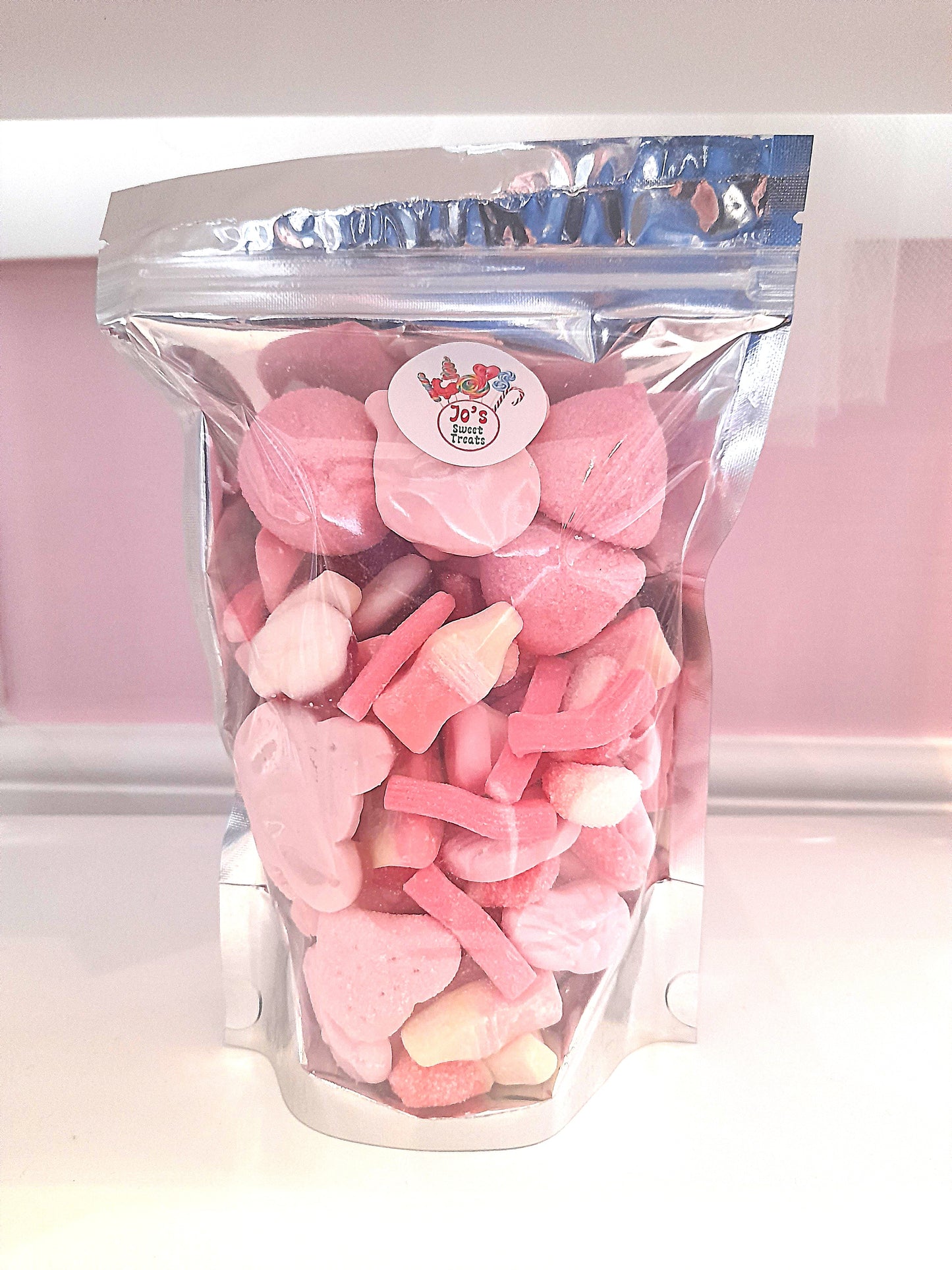 A clear plastic bag filled with various pink and white candy pieces, with a label showing the product name and a website.