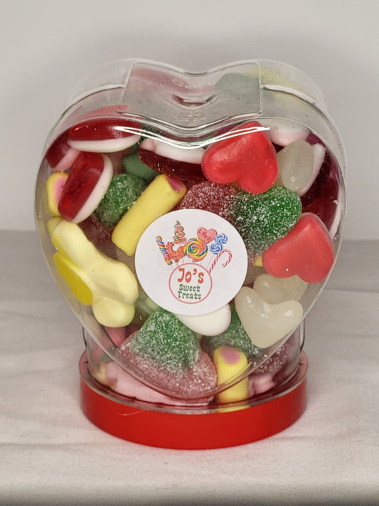 A heart-shaped plastic jar with a red screw-top lid, filled with various colorful candies.