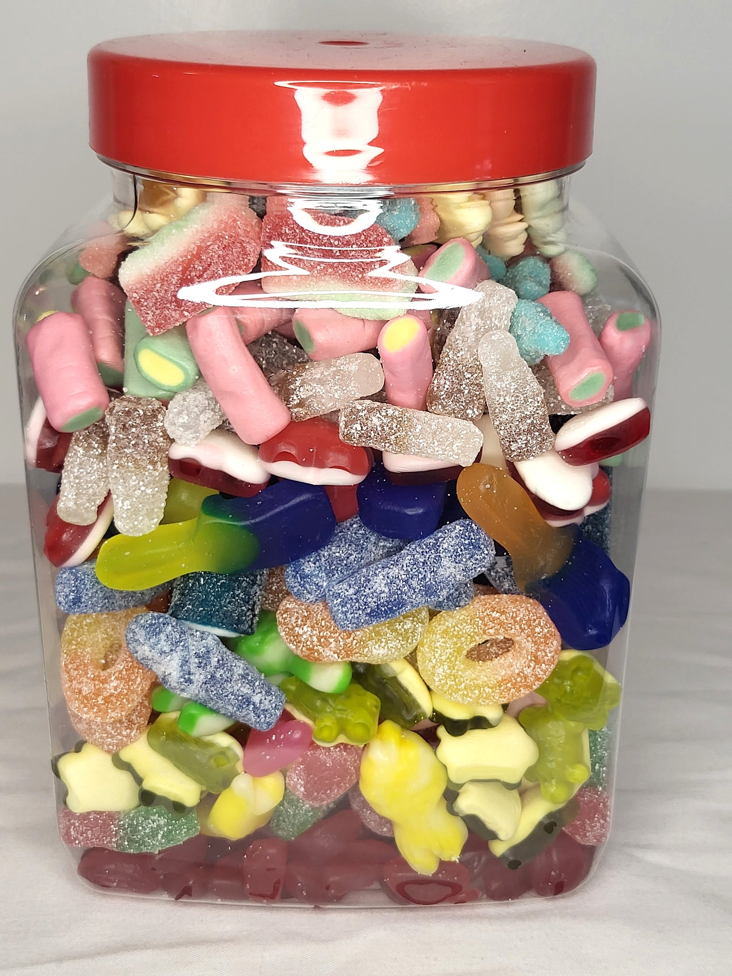 A medium-sized clear jar filled with a variety of colorful candies, sealed with a red lid.